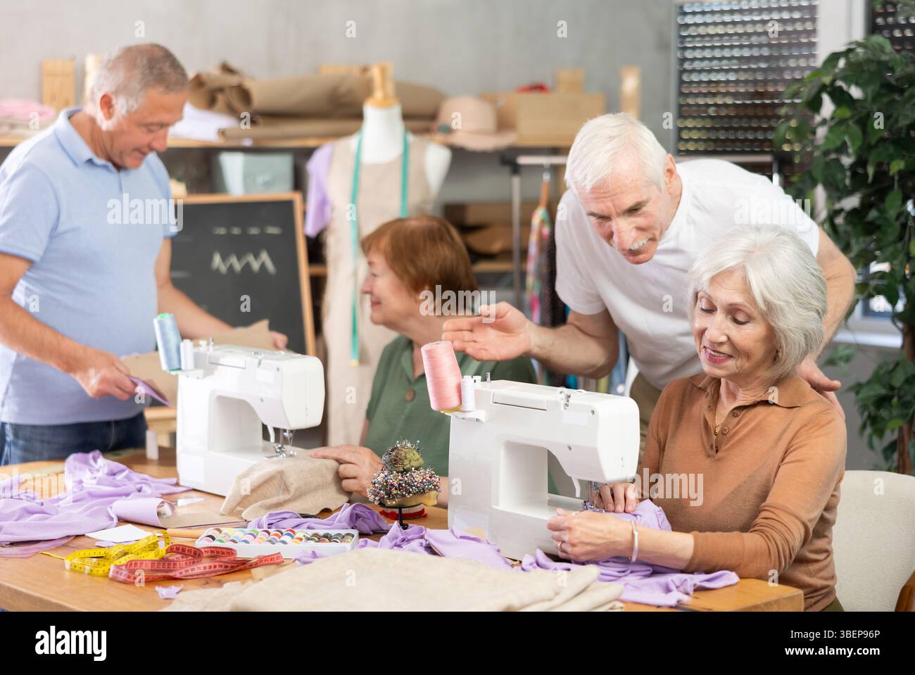 Some people communicate and discuss pattern, while others sew using sewing machine at lesson Stock Photo
