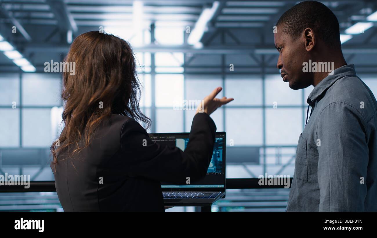 AI technology used by data center software developers reviewing equipment diagnostics. Programmers coding on laptop using artificial intelligence, adjusting server farm configurations, camera A Stock Photo