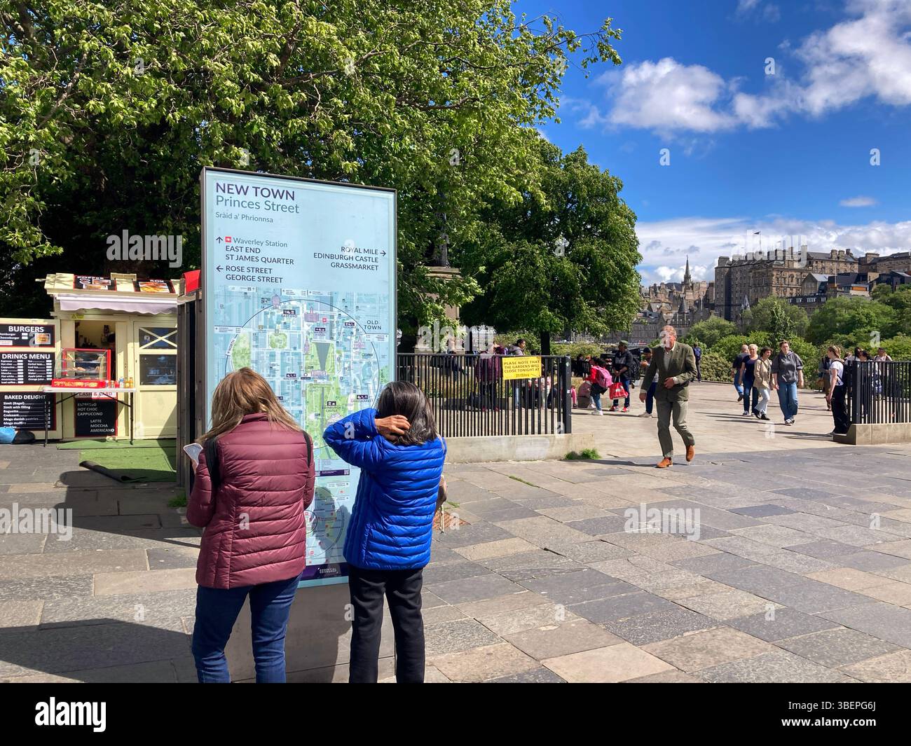 Visitors checking the information board with city map and attractions on Princes Street at The Mound Precinct, Edinburgh Scotland - Smartphone Captured Stock Image