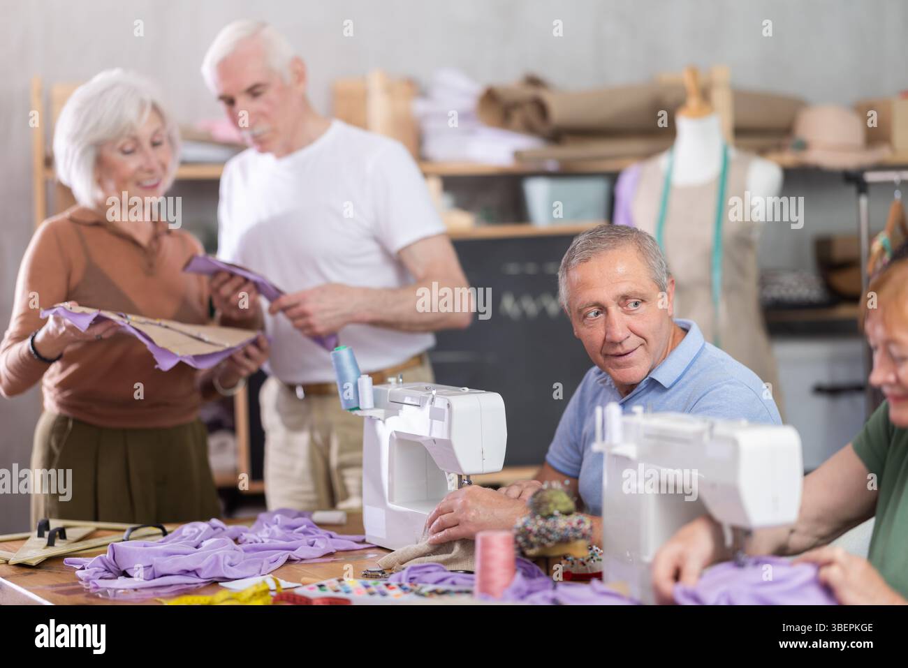 Some people communicate and discuss pattern, while others sew using sewing machine at lesson Stock Photo