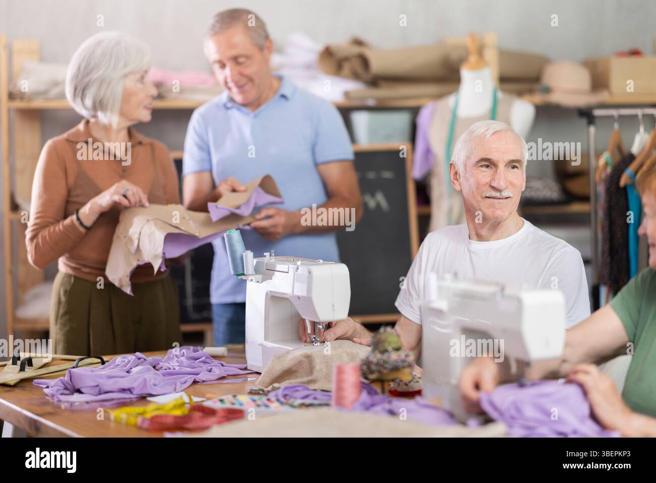 Some people communicate and discuss pattern, while others sew using sewing machine at lesson Stock Photo