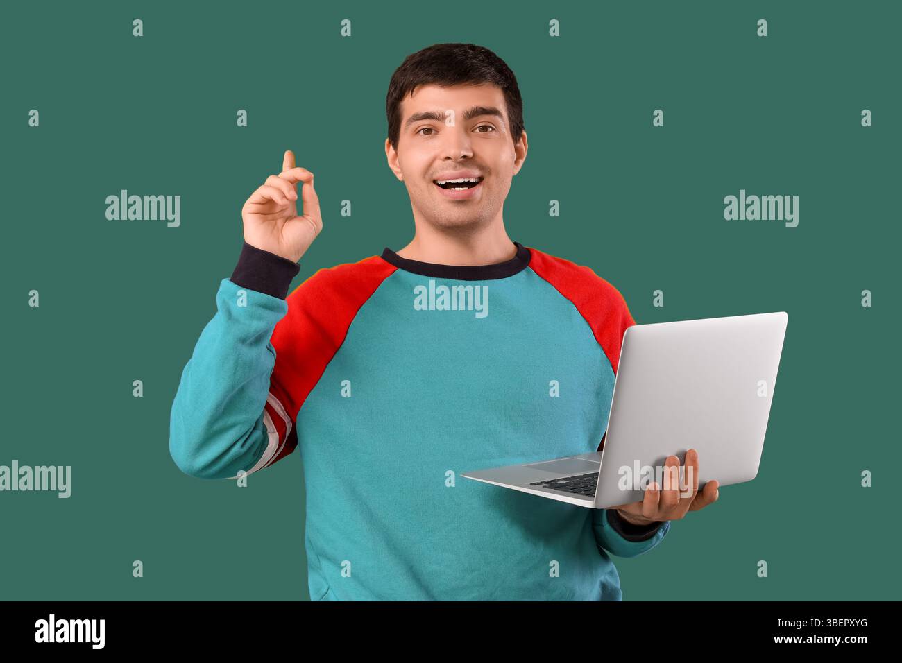 Male programmer with laptop pointing at something on green background Stock Photo