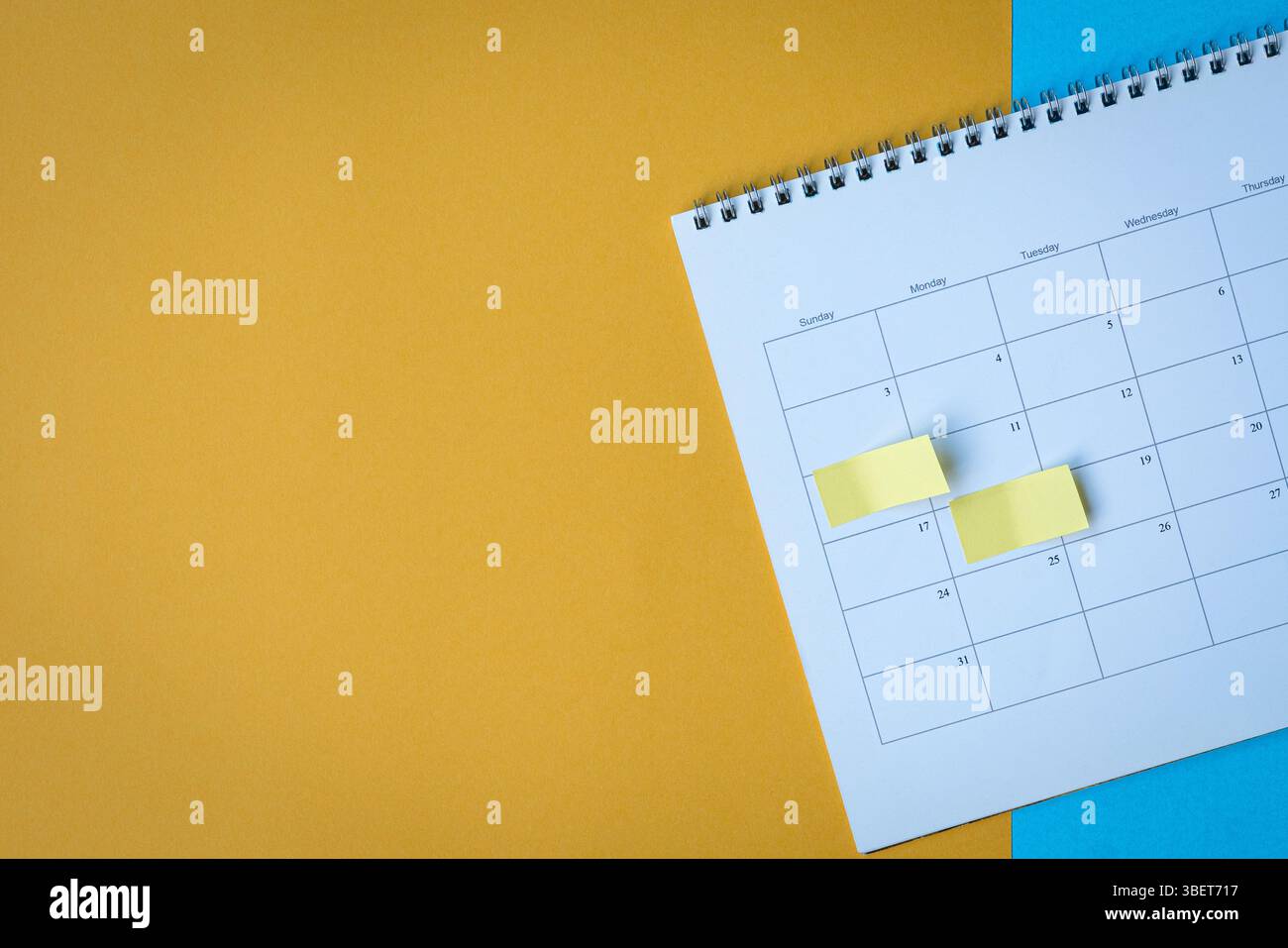 Calendar page with yellow adhesive notes. On top of blue and yellow surface. Copy space. Stock Photo