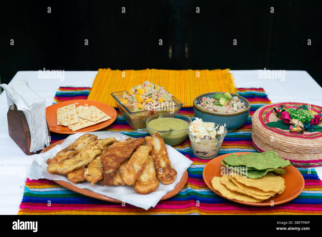 A vibrant table displays an array of Mexican appetizers: fresh salsas, crispy fried fishes, tortilla chips and ceviche. Stock Photo