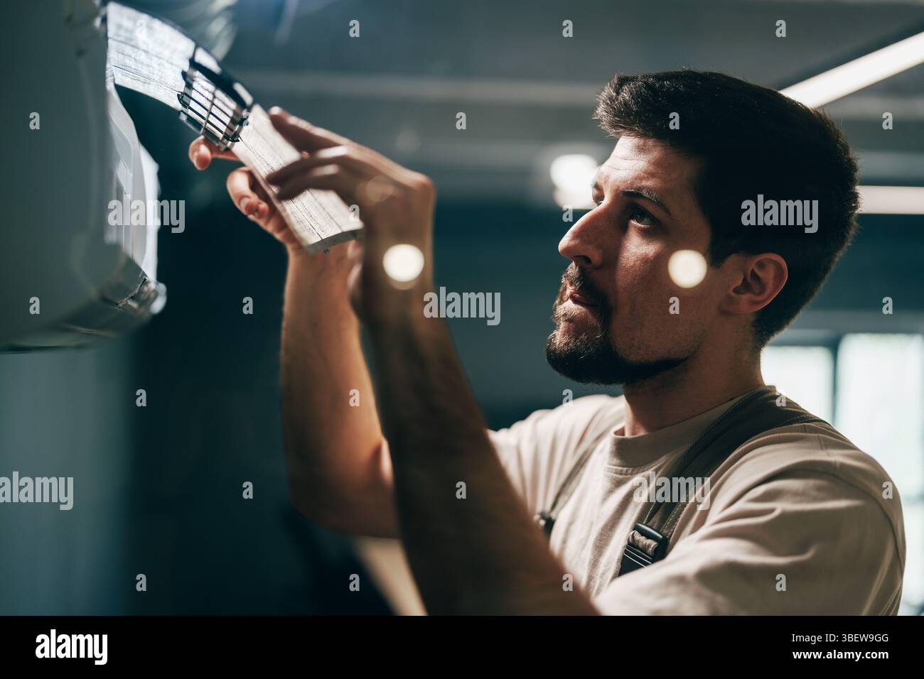 Man performs maintenance on air conditioning unit inside modern building during daylight Stock Photo
