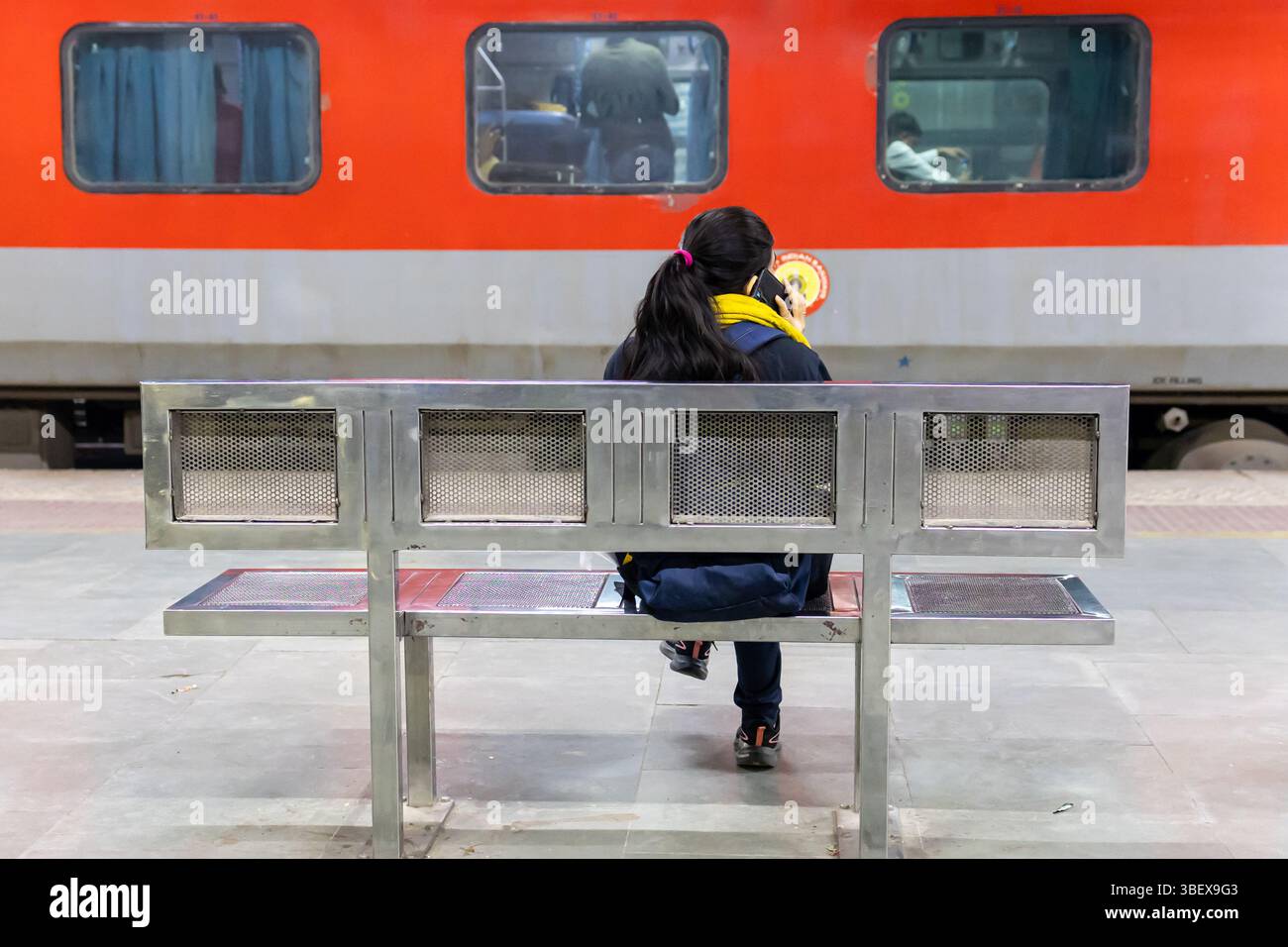 isolated girl sitting at iron bench to catch the train at evening with ...