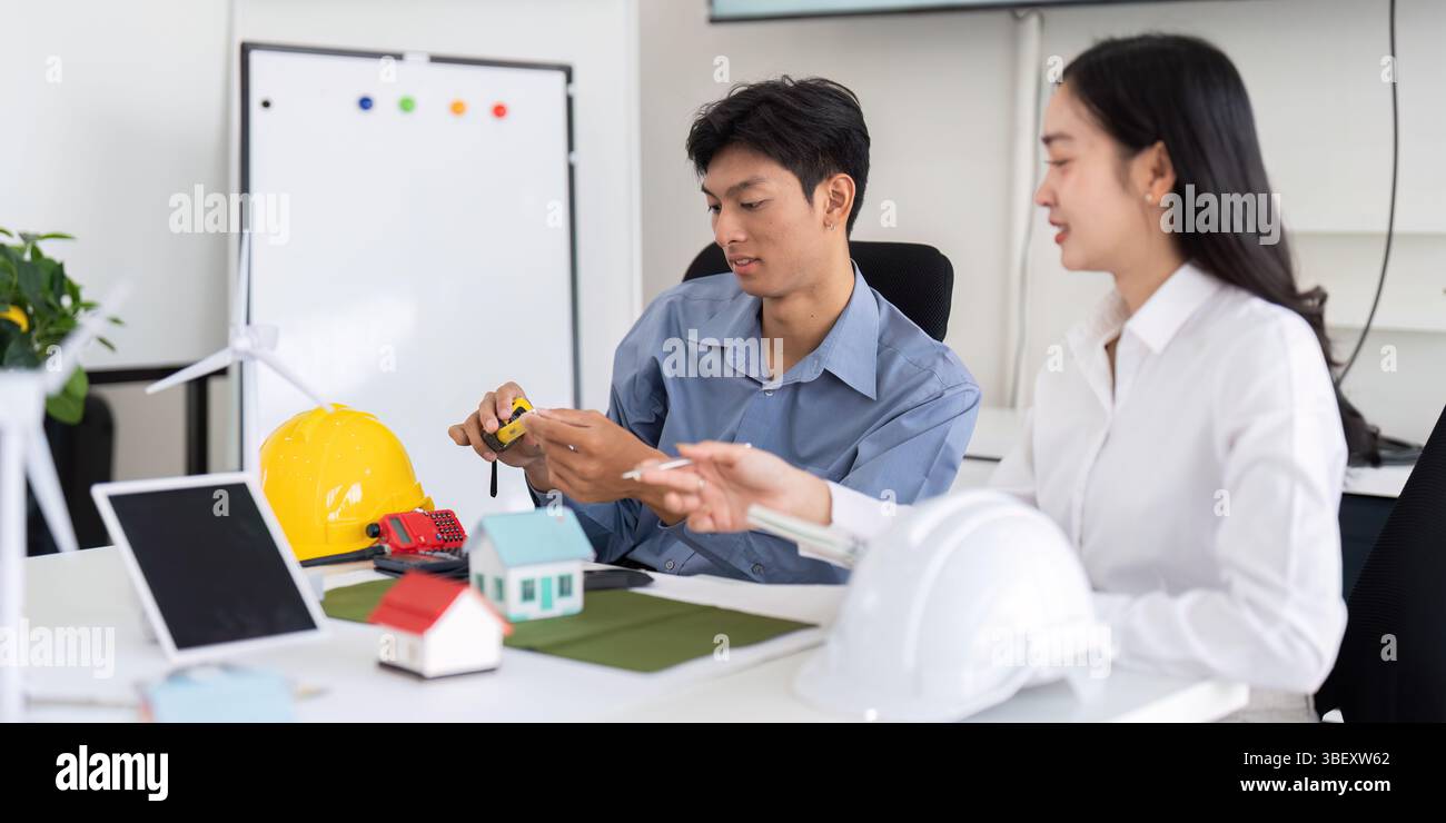 Sustainability and Engineering. Two engineers discussing eco-friendly design solutions with models and tools. Stock Photo