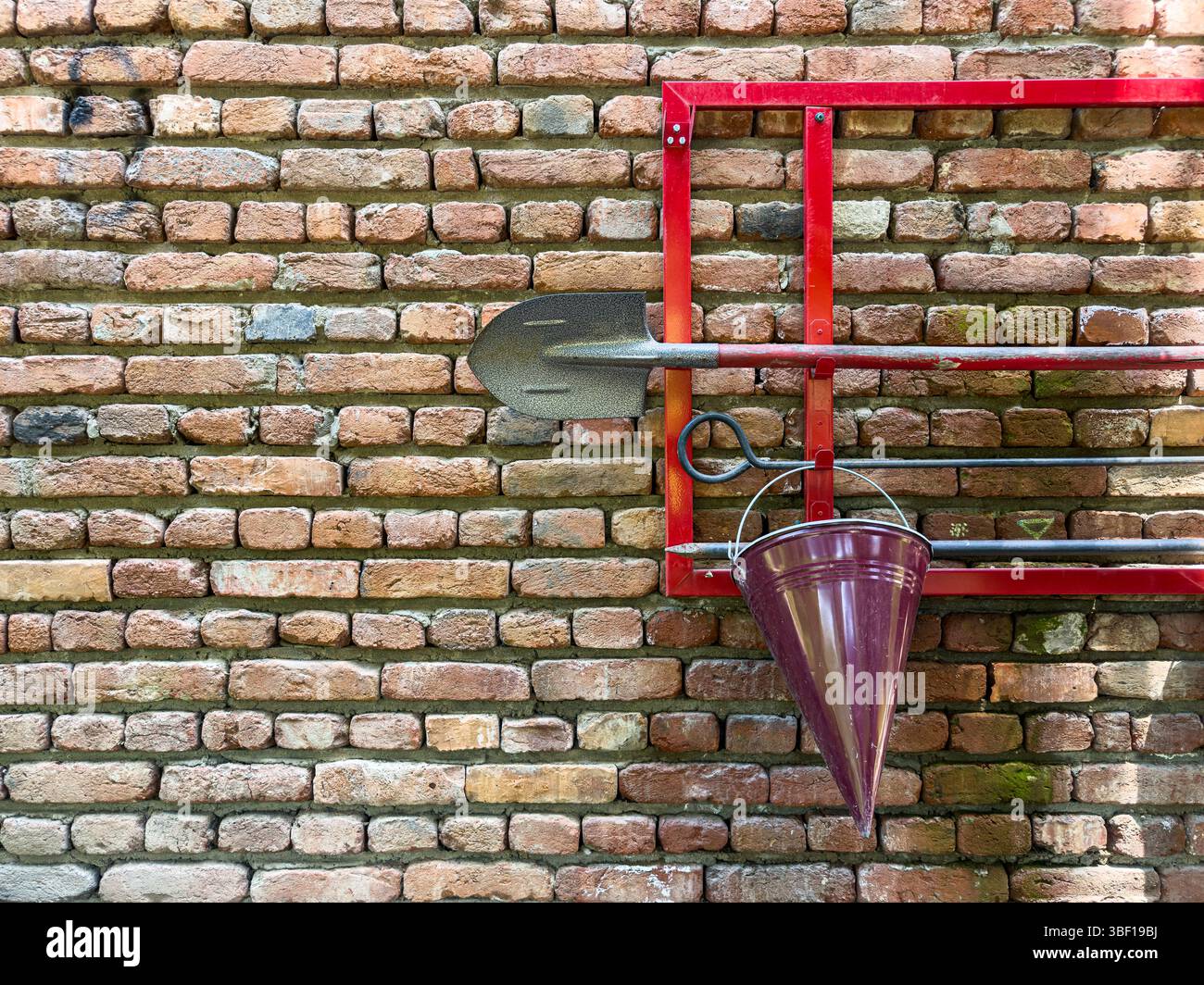 Firefighting set on brick wall with red metal frame, conical bucket, shovel and hook, safety equipment for emergency use, workplace and public safety. Stock Photo