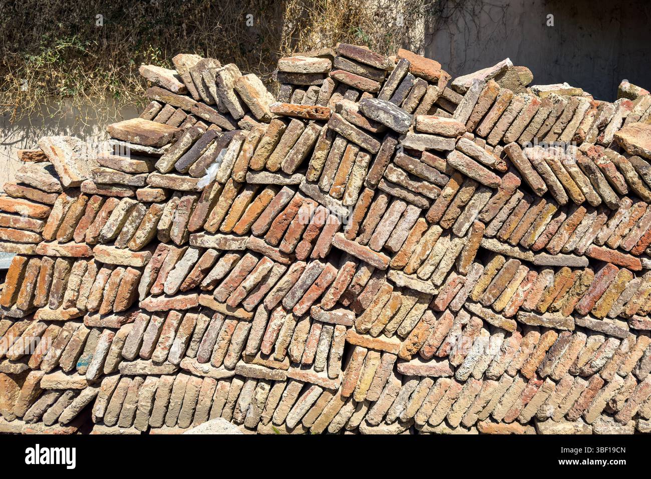 Stack of old clay bricks in irregular pattern, construction material background, building industry texture, rustic surface, no people. Stock Photo