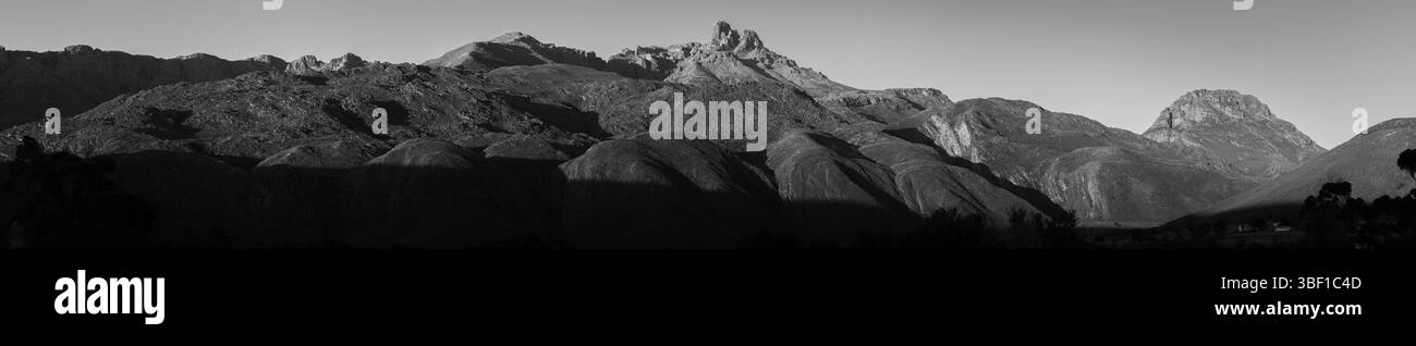 A dramatic panoramic black and white view of a South African mountain range, captured at sunrise with sweeping shadows and rich tonal contrast. Stock Photo