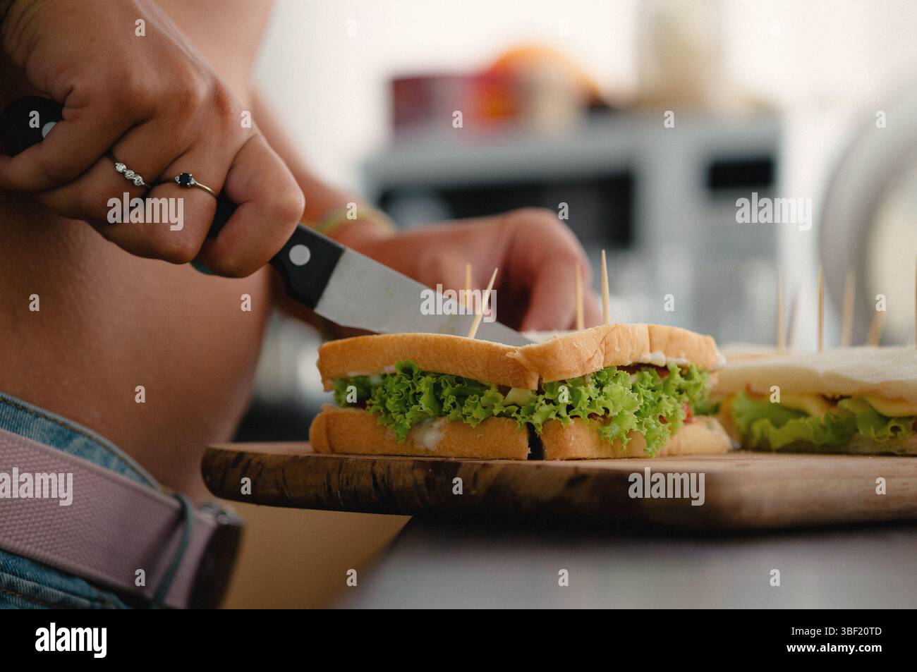 Person slicing fresh sandwich with lettuce and tomato Stock Photo