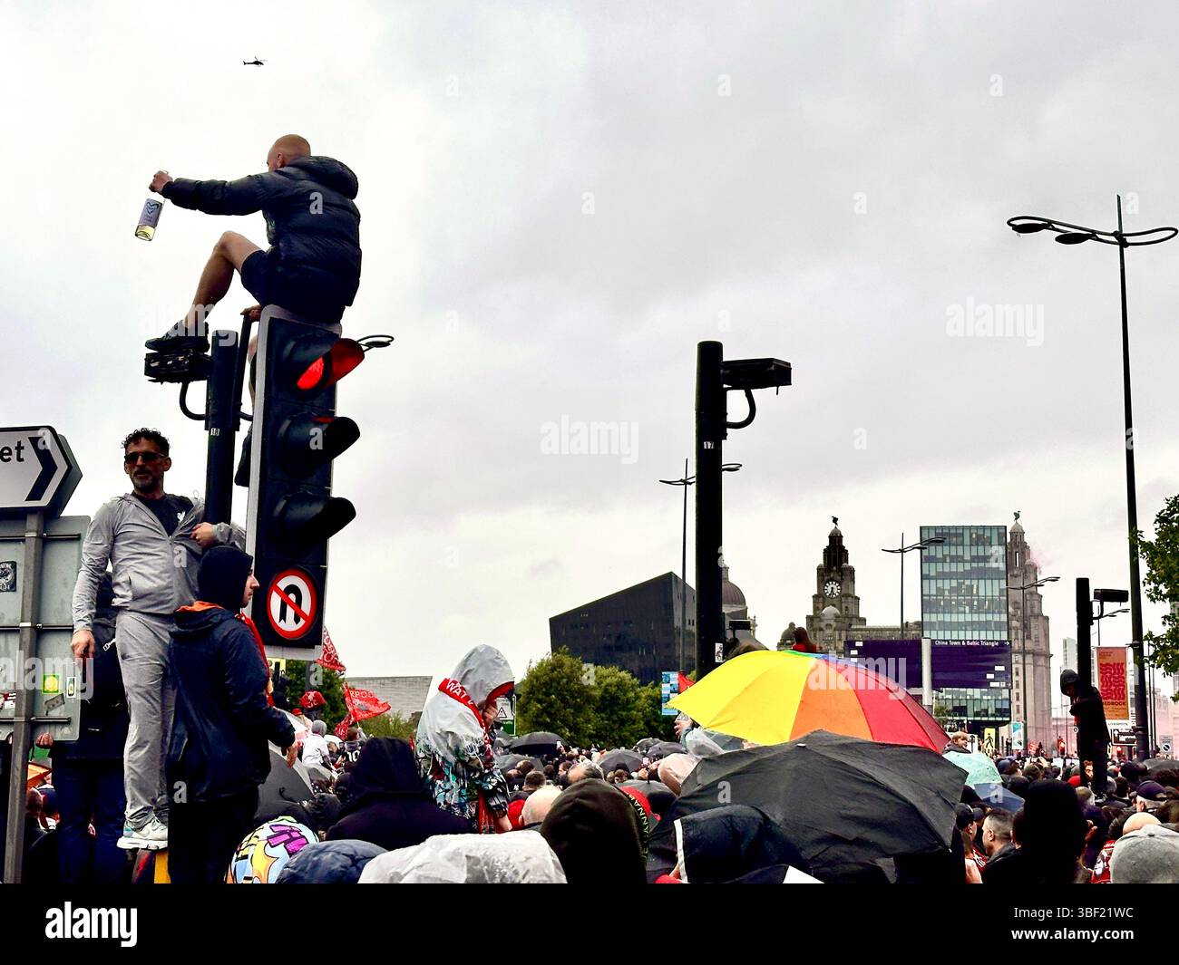 Supporters gather on The Strand with umbrellas and fans on traffic lights with Liver Buildings rise in the background during Liverpool parade, 25 May - Smartphone Captured Stock Image