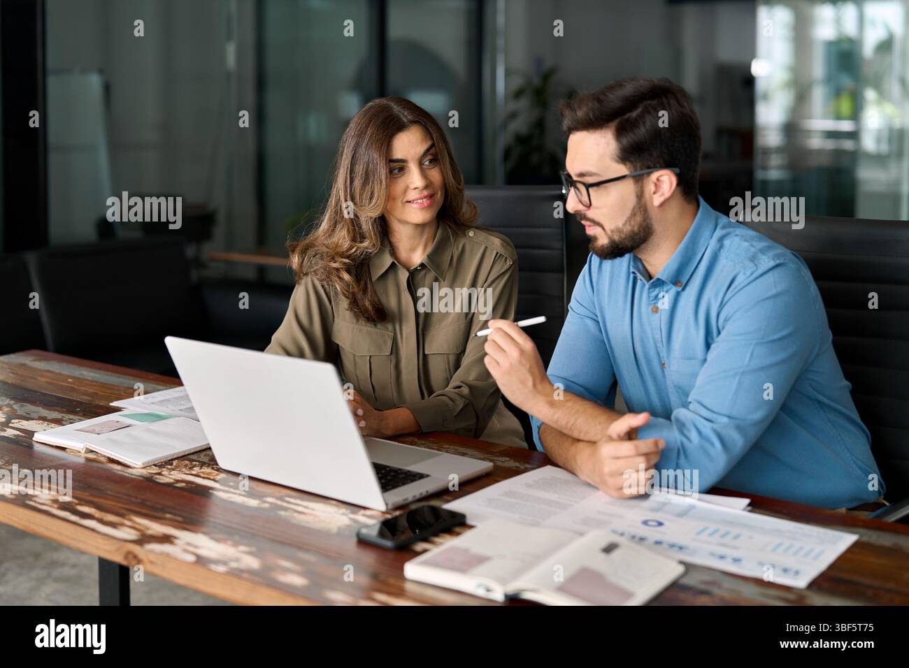 Two busy colleagues working together talking using laptop in office. Stock Photo