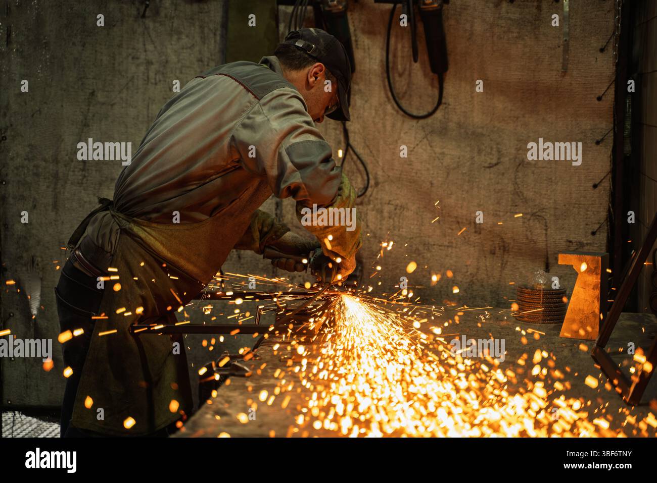 Industrial Metalworker Using Angle Grinder in Workshop with Flying Sparks Stock Photo
