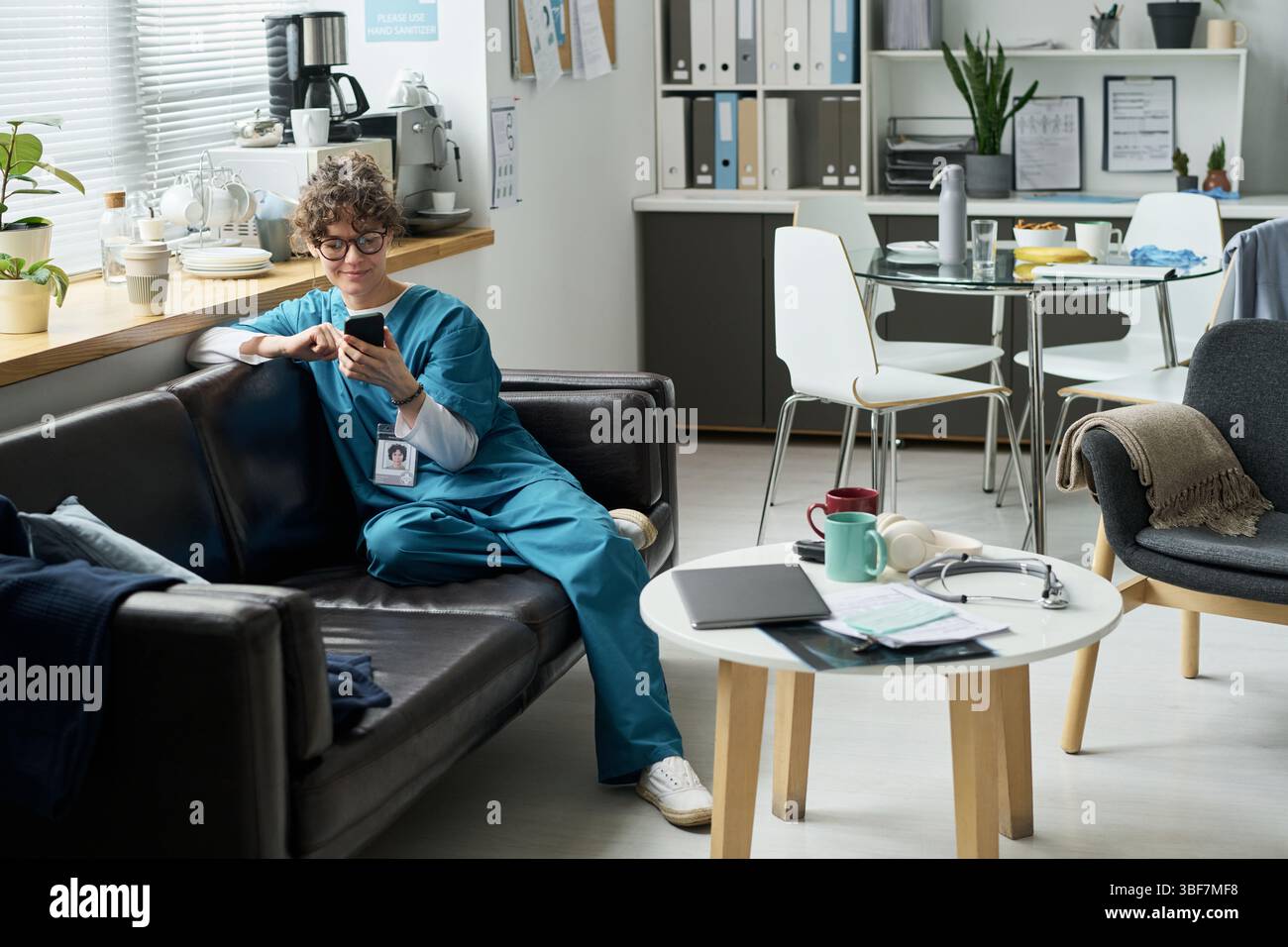 Female nurse taking break on couch in hospital break room while holding ...