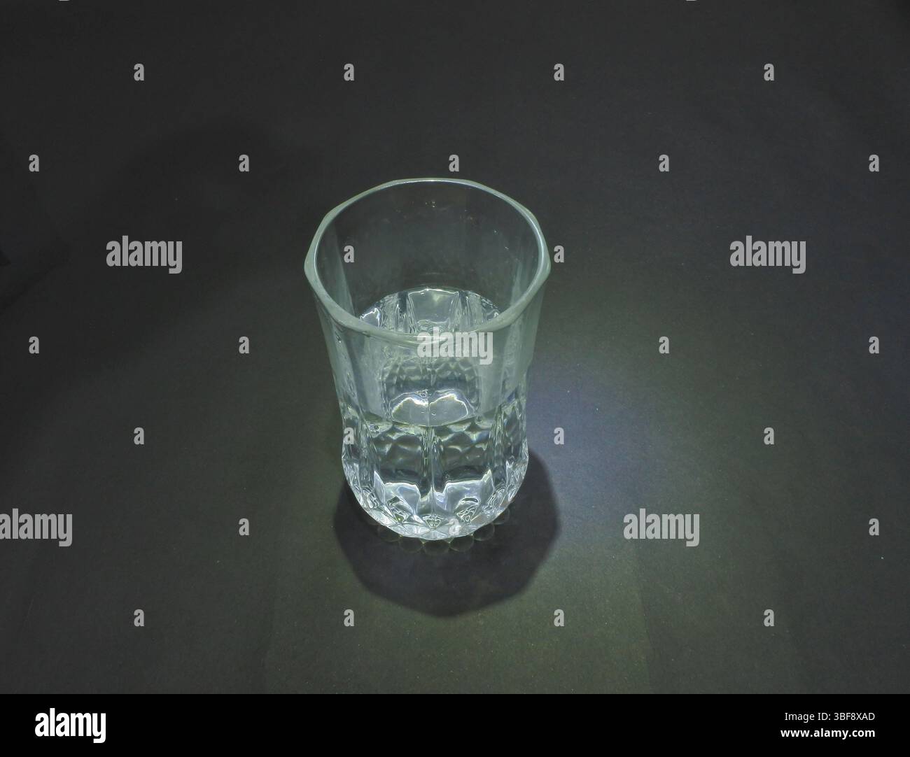 Half a glass of clear water is placed in the black background area. Stock Photo