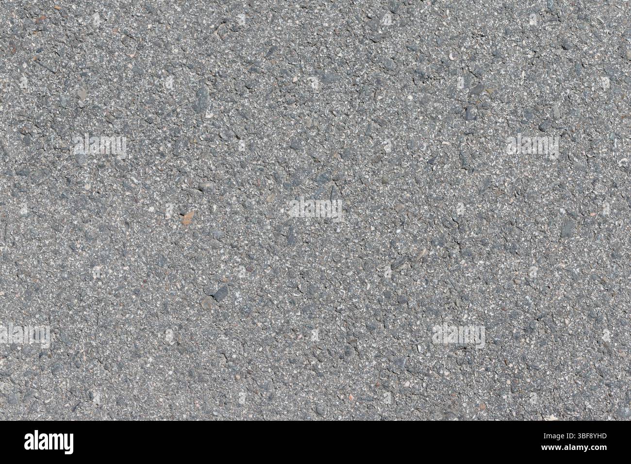 A close-up shot of gray asphalt. Small pebbles and gravel are embedded ...