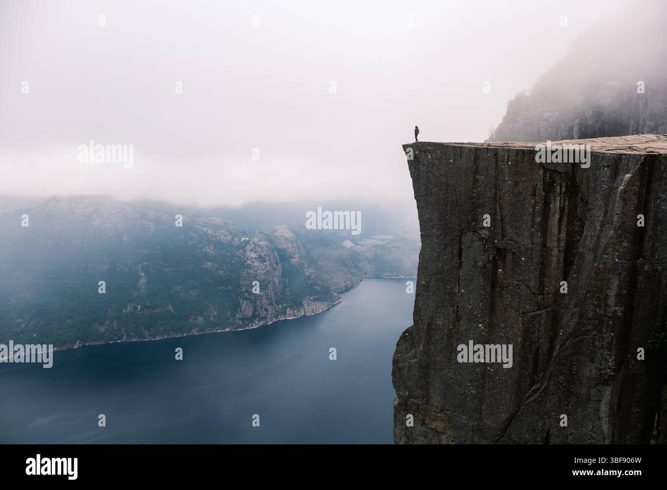A solitary figure stands on the edge of a dramatic cliff, gazing out ...