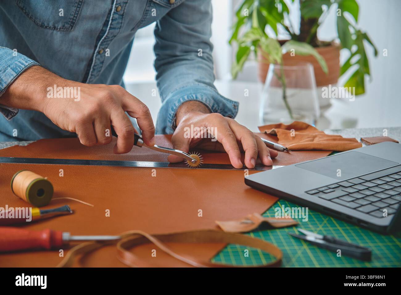 Craftsman using stitching groover and ruler to work leather in his workshop Stock Photo