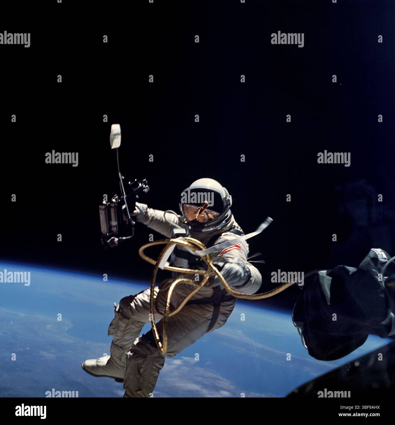 Astronaut Edward H. White II floats during America's first spacewalk on 3 June 1965, part of the Gemini 4 mission. He spent 23 minutes manoeuvring outside the spacecraft using a Hand-Held Self-Maneuvering Unit (HHSMU), while Jim McDivitt remained inside. White was tethered by a 25-ft umbilical and 23-ft tether wrapped in gold tape. His helmet visor was gold-plated to shield against the Sun's rays. Optimised NASA image. Credit: NASA. Editorial use only. Stock Photo