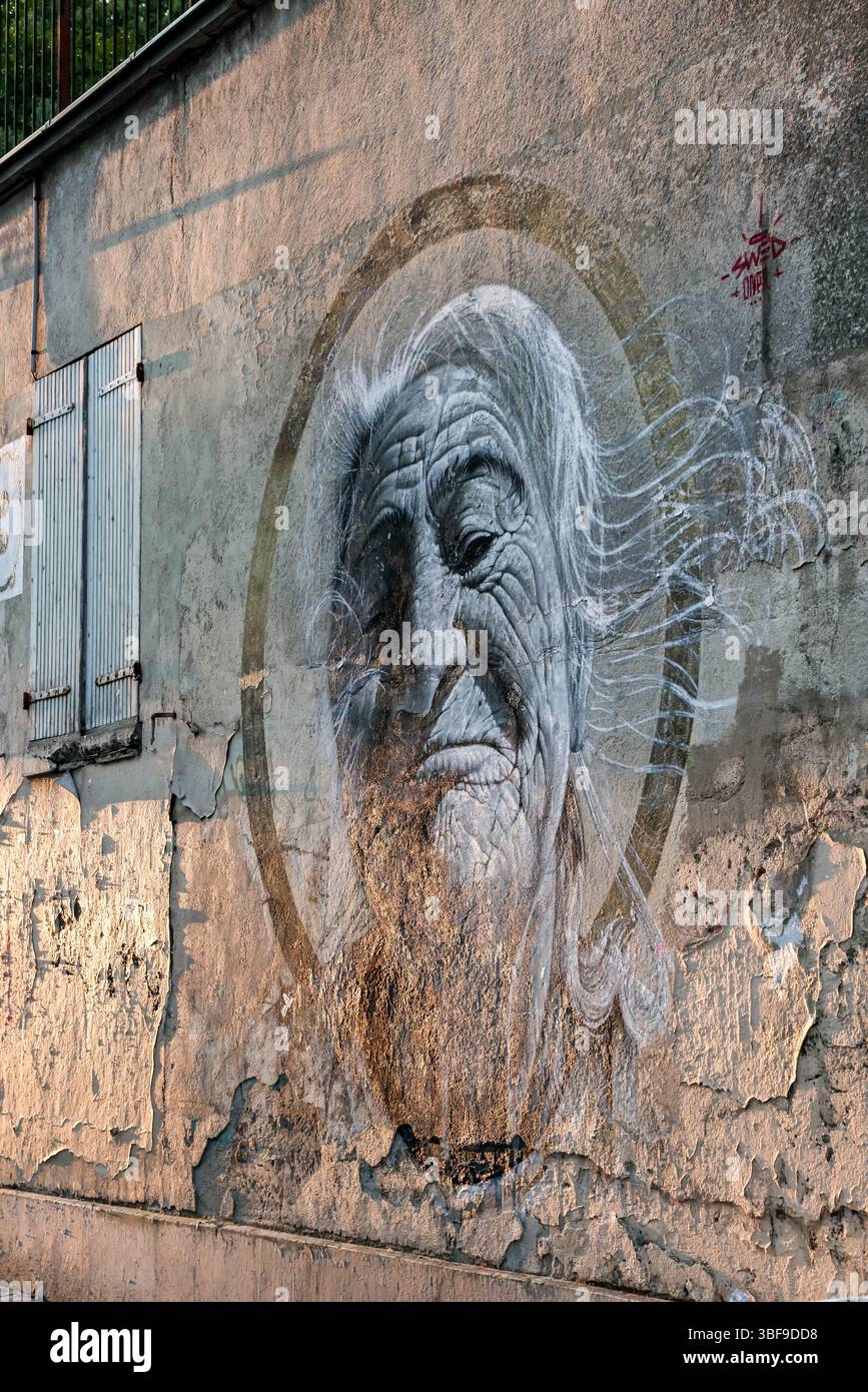 A powerful and evocative monochrome street art portrait painted on a weathered, textured urban wall. The detailed and expressive face in the mural add Stock Photo