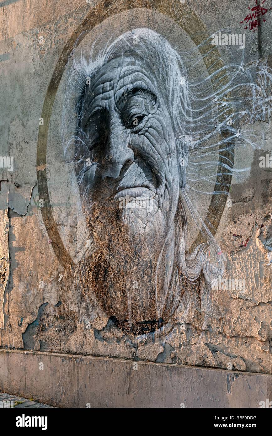 A powerful and evocative monochrome street art portrait painted on a weathered, textured urban wall. The detailed and expressive face in the mural add Stock Photo