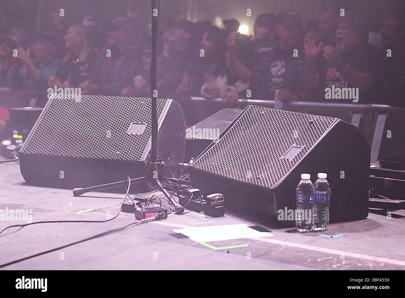 A pair of stage monitors, a microphone stand & 2 bottles of water on a stage as the audience awaits the entrance of a band at the Bonfest 2025. Stock Photo
