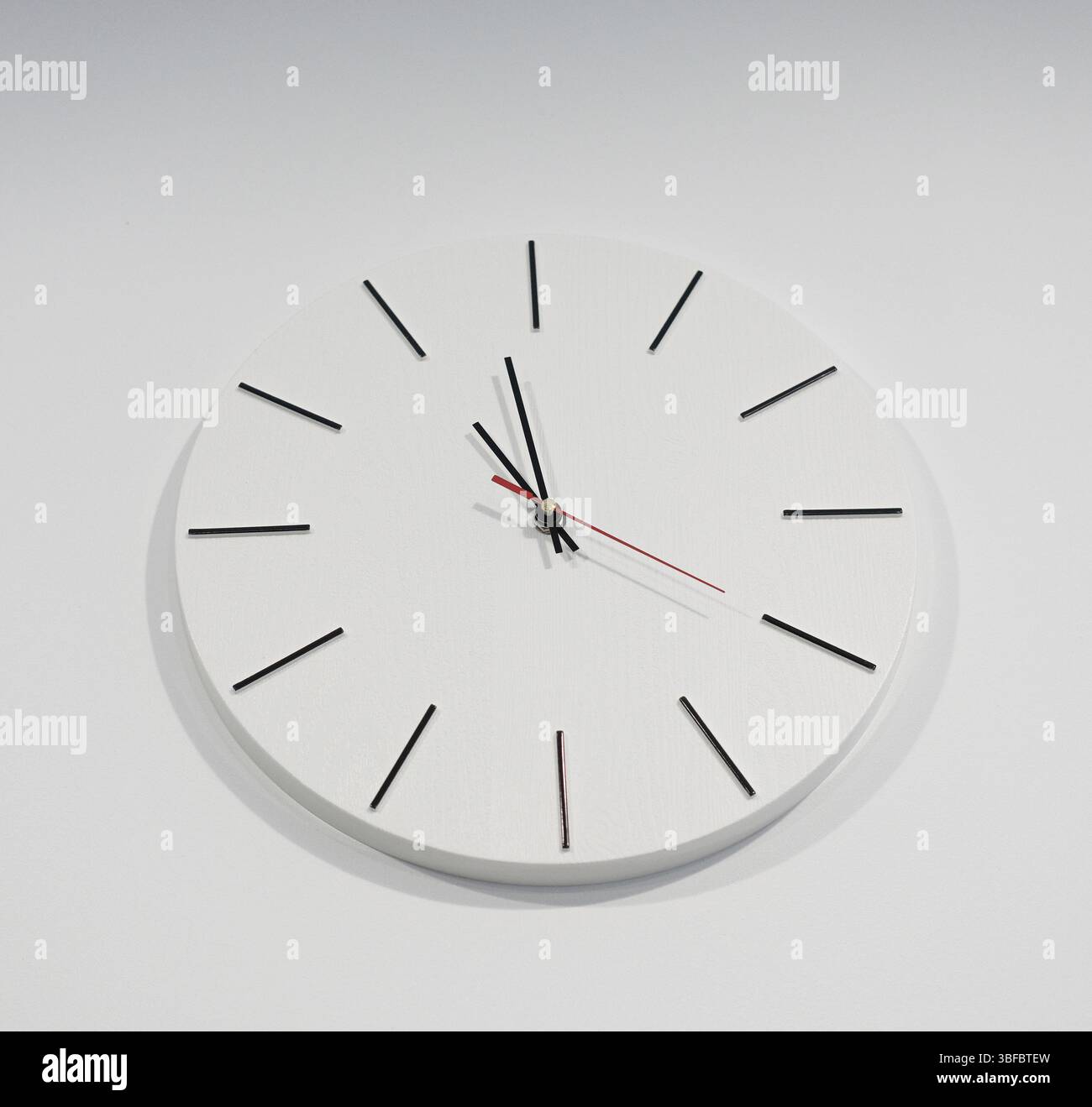 White round clock hangs on a light wall Stock Photo