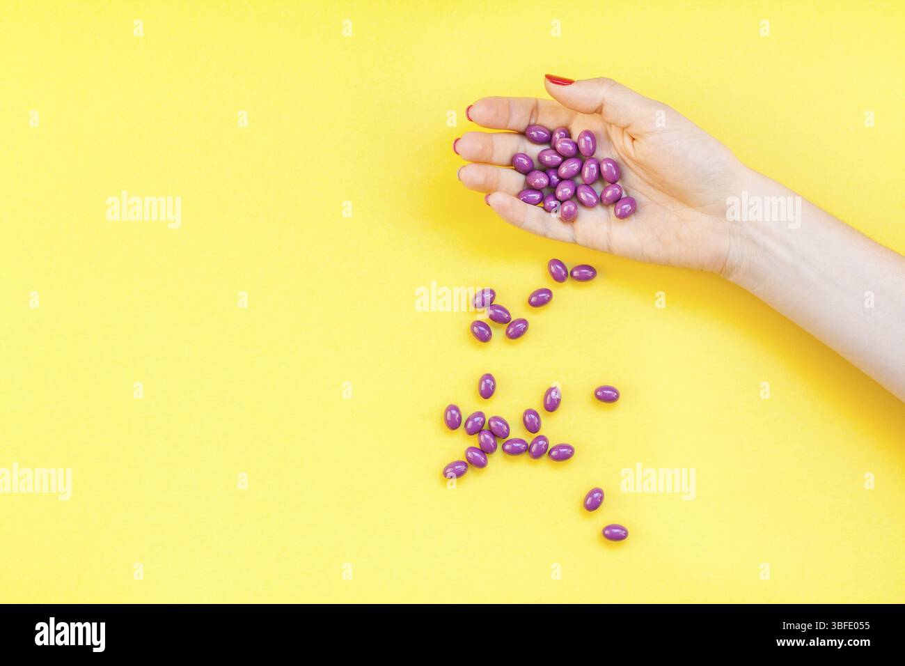 Woman hand holding purple pills handful isolated on bold yellow background with copy space. Template for feminine beauty blog social media. Female hea Stock Photo