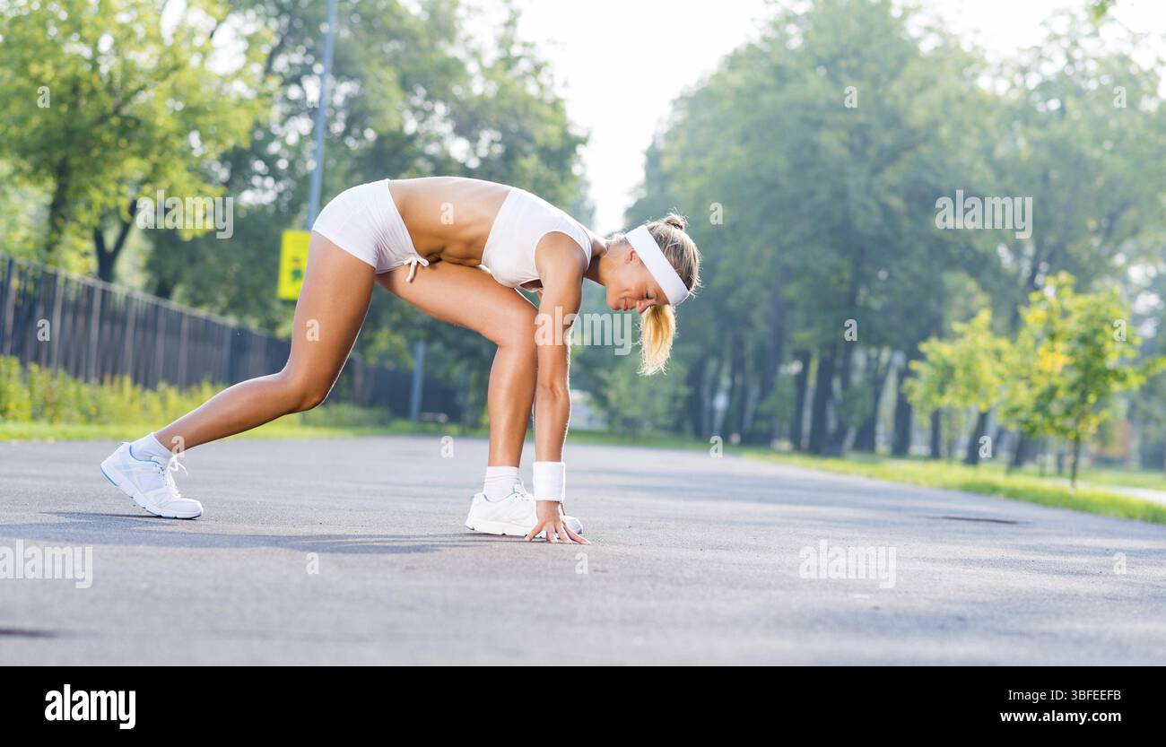 Young woman runner outdoor standing in start pose Stock Photo