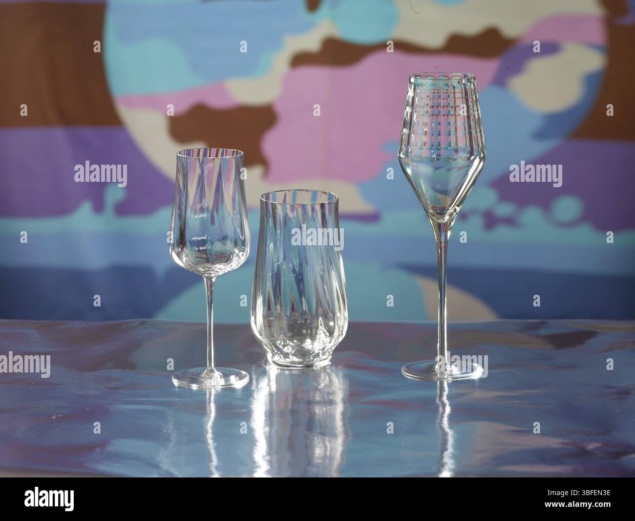 Various glasses on silver foil, behind them various colour elements, studio shot Stock Photo