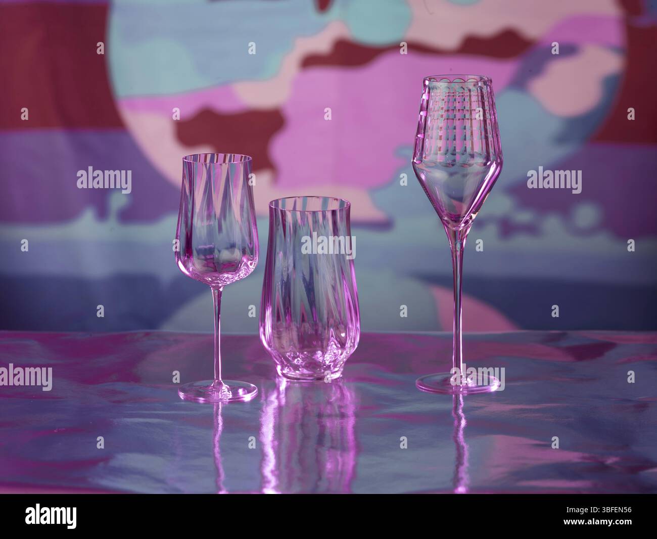 Various glasses on silver foil, behind them various colour elements, studio shot Stock Photo