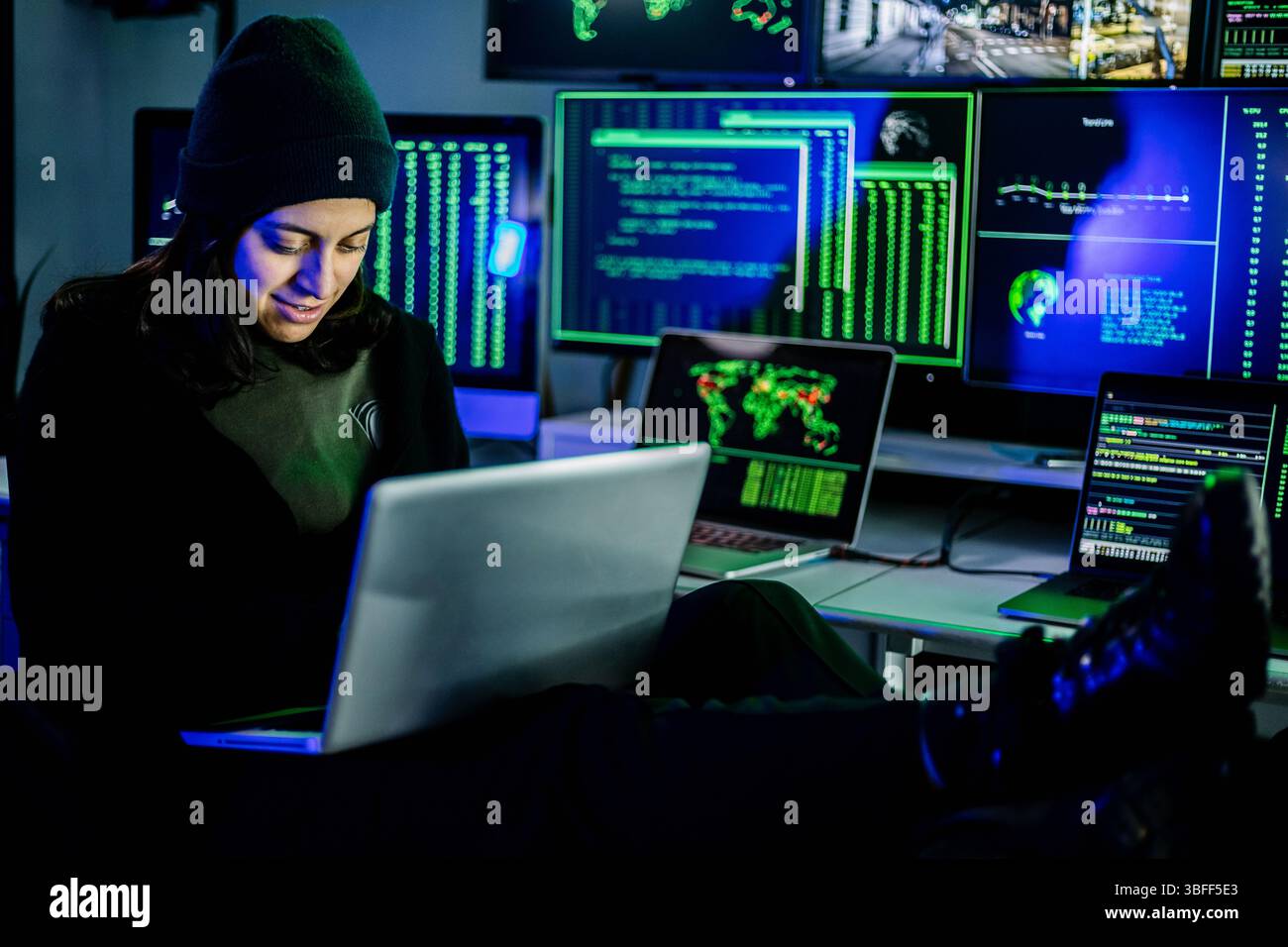 Female hacker breaking into corporate network using laptop and multiple screens Stock Photo
