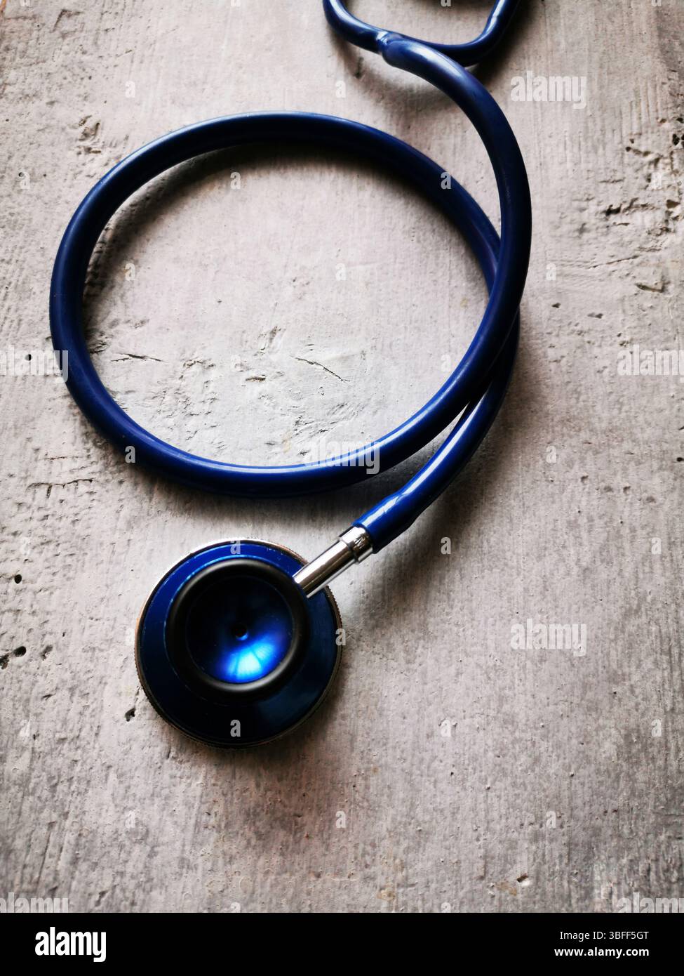 A blue stethoscope lies on a textured surface, its reflection catching the light in a clinical setting. - Smartphone Captured Stock Image