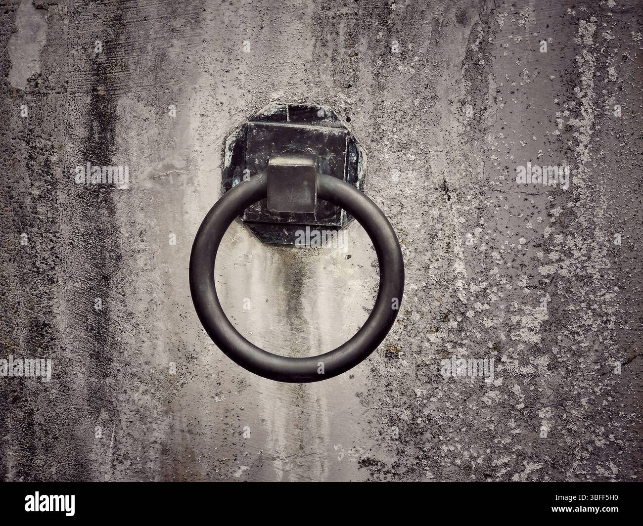 A weathered wall features a rusty metal ring affixed to it, suggesting a historical purpose. The texture and color highlight the passage of time - Smartphone Captured Stock Image
