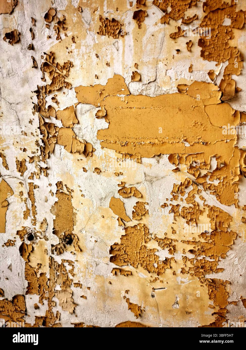 This textured wall features layers of peeling paint in warm yellow and beige tones, revealing the underlying material. - Smartphone Captured Stock Image