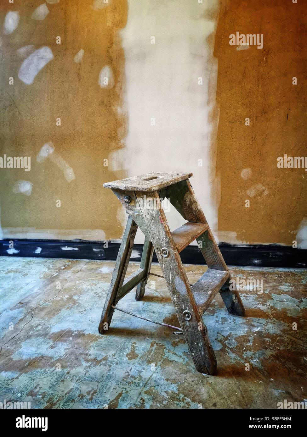 A worn wooden ladder rests on an uneven floor in a room with a freshly painted wall. The surroundings indicate ongoing home improvement work - Smartphone Captured Stock Image