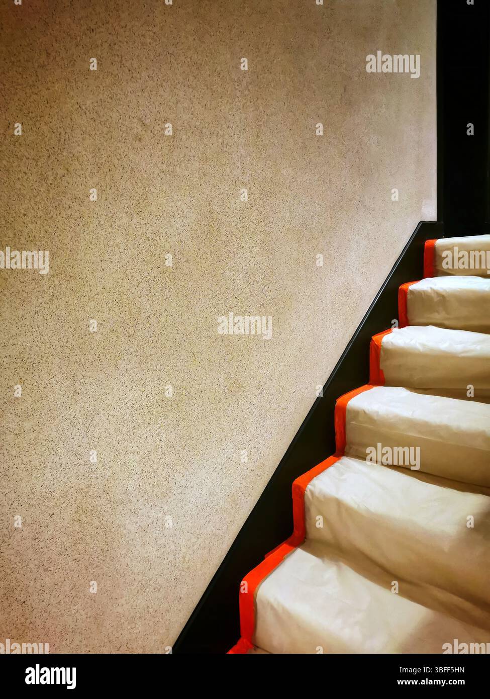 A staircase featuring smooth, soft white steps contrasted by bold orange edges. The surrounding wall is a subtle beige - Smartphone Captured Stock Image