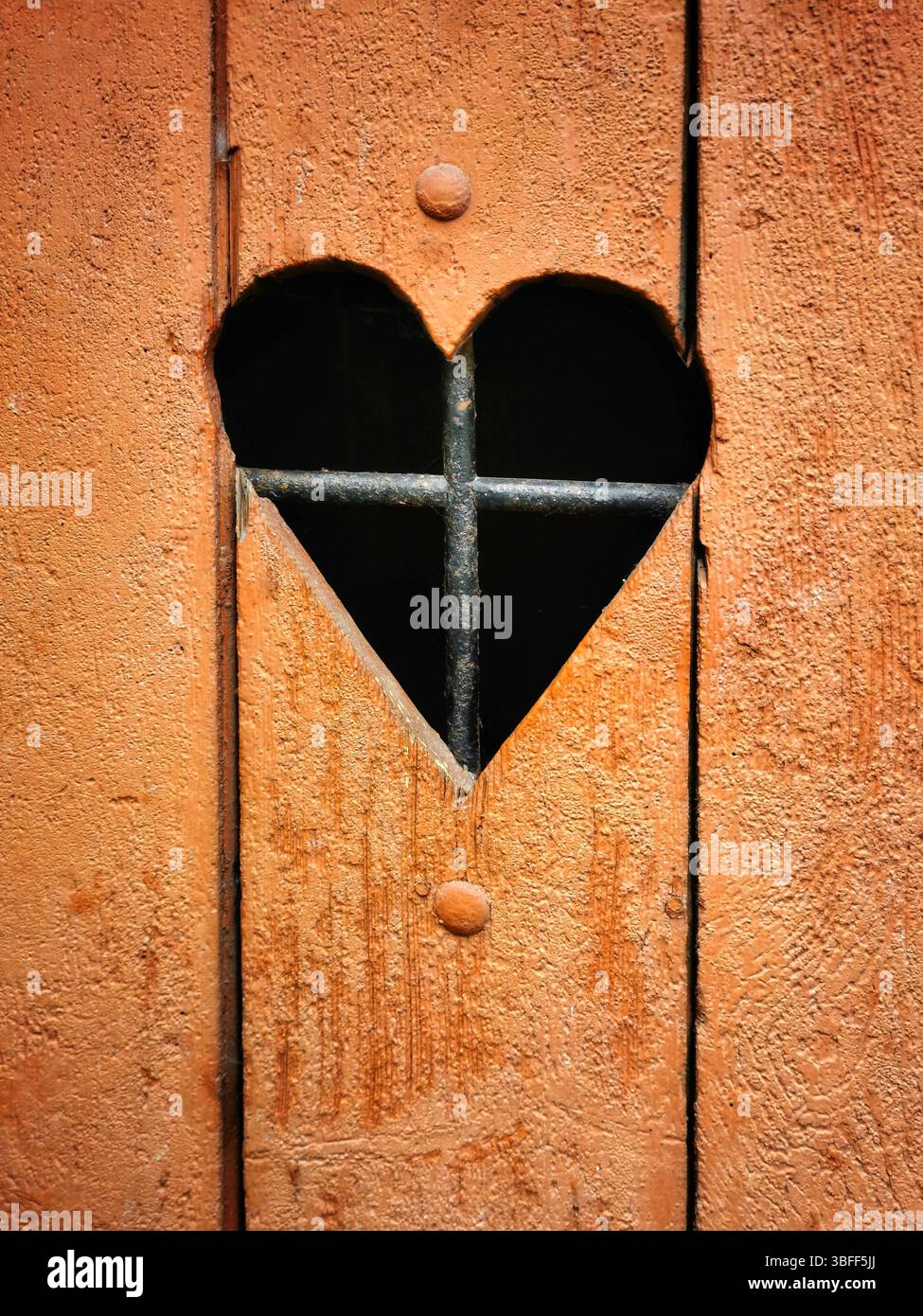 A rustic wooden door features a heart-shaped cutout that reveals iron bars behind it. - Smartphone Captured Stock Image