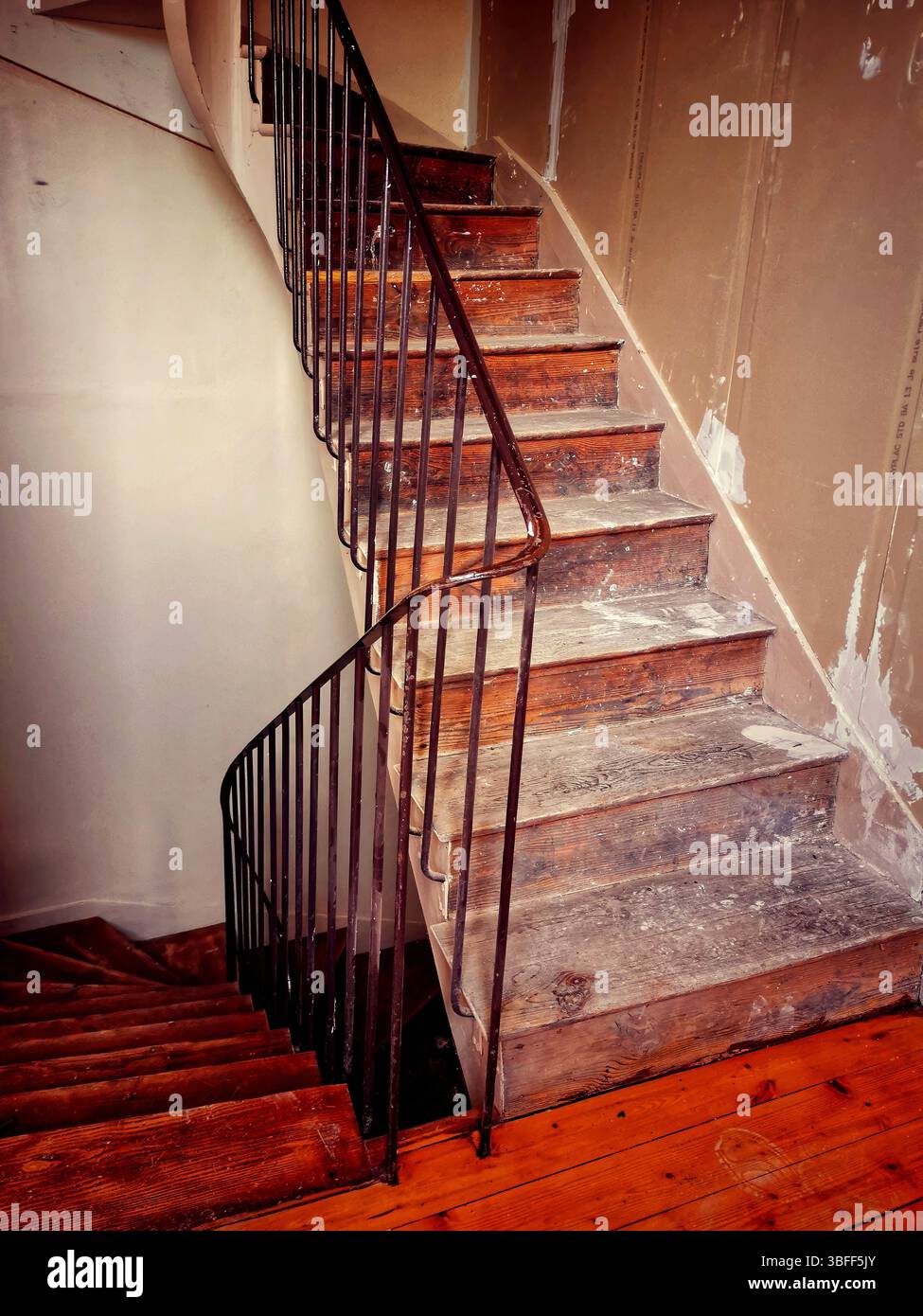 A winding staircase constructed from rustic wood features elegant iron railings, set in a partially renovated interior with unfinished walls. - Smartphone Captured Stock Image