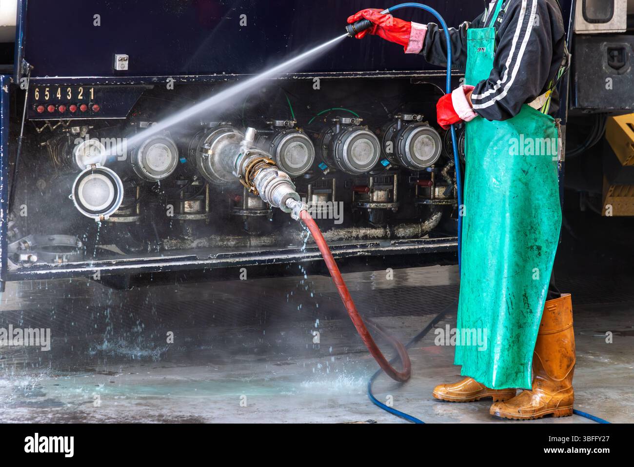 Operator at a tanker truck wash station cleaning the discharge outlet ...
