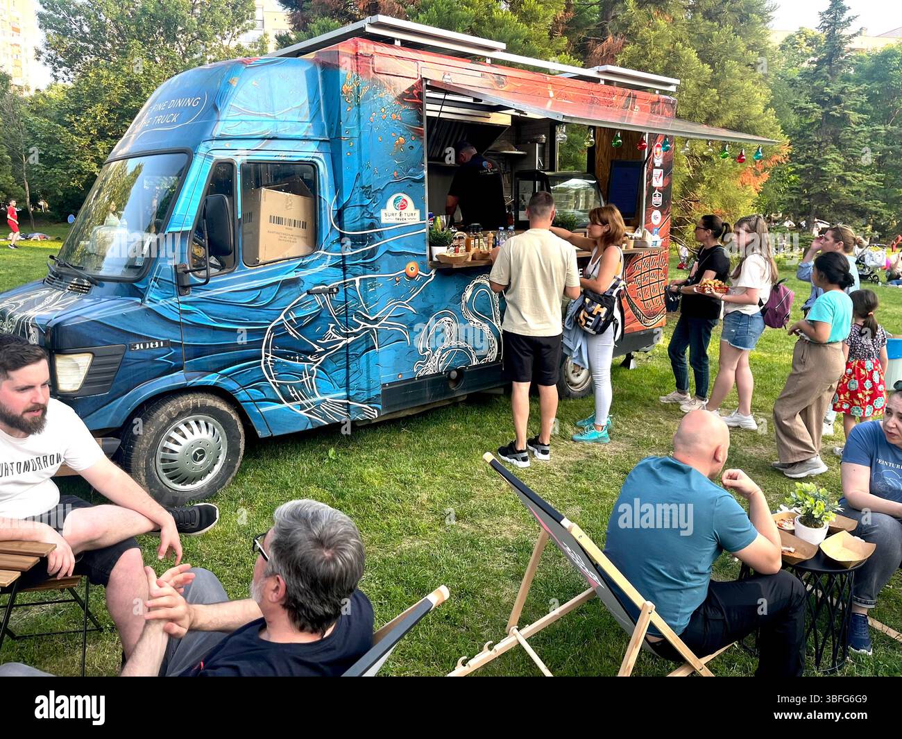Street food truck serving surf and turf dishes at an urban garden party, offering grilled meat options to event-goers in a casual outdoor setting - Smartphone Captured Stock Image