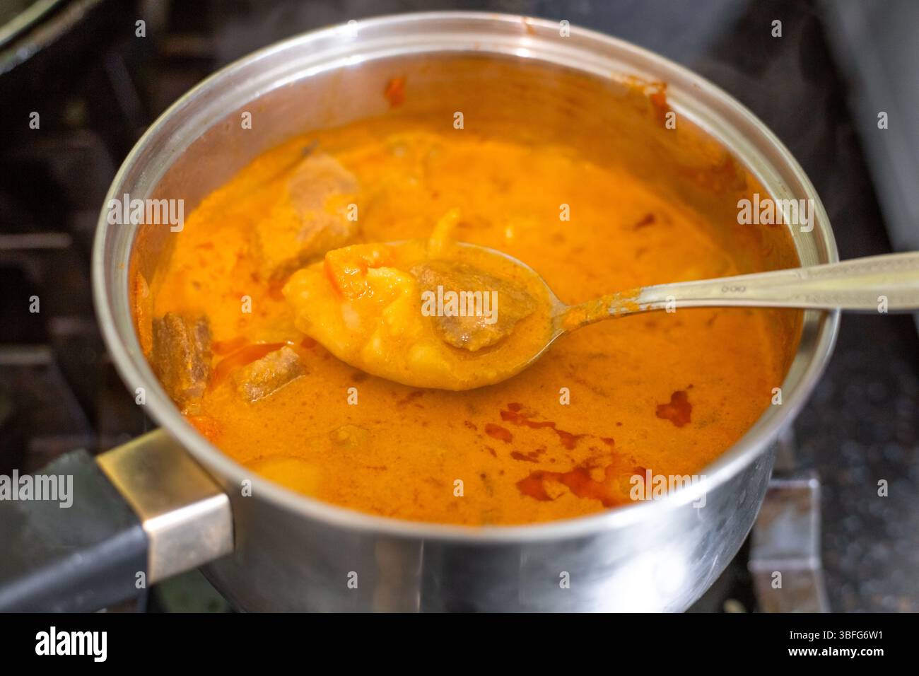 Making massaman curry. Stirring the dish with a spoon in a saucepan on the stove. Stock Photo