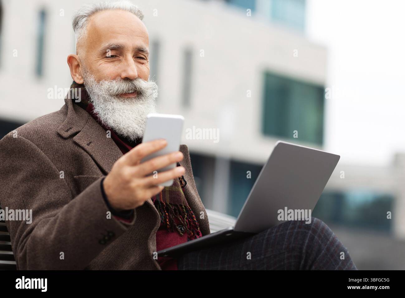 Senior businessman with laptop using smartphone outdoors Stock Photo