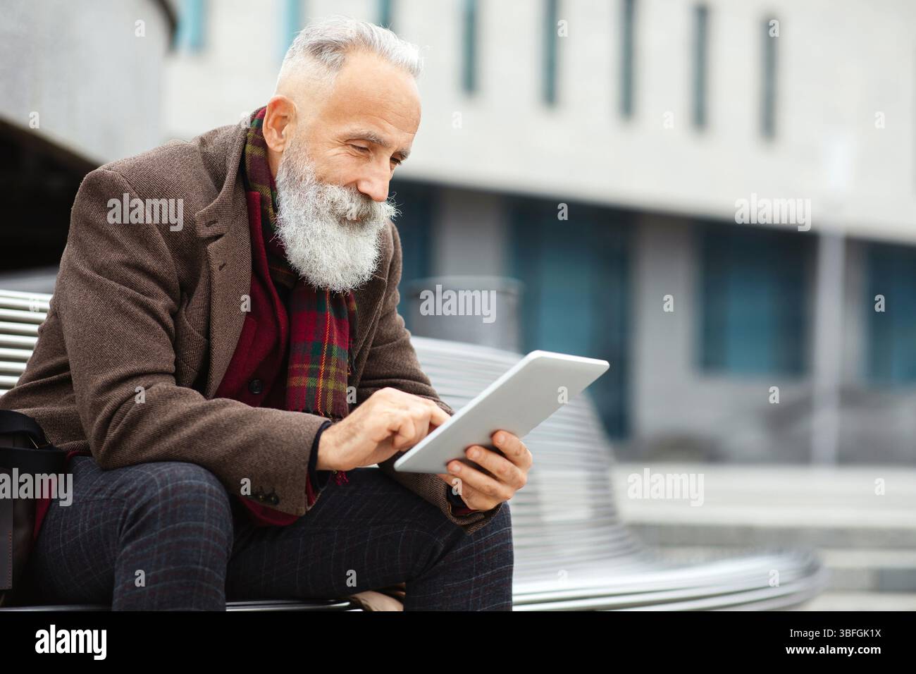Stylish grey-haired man sitting on the bench, using digital tablet Stock Photo