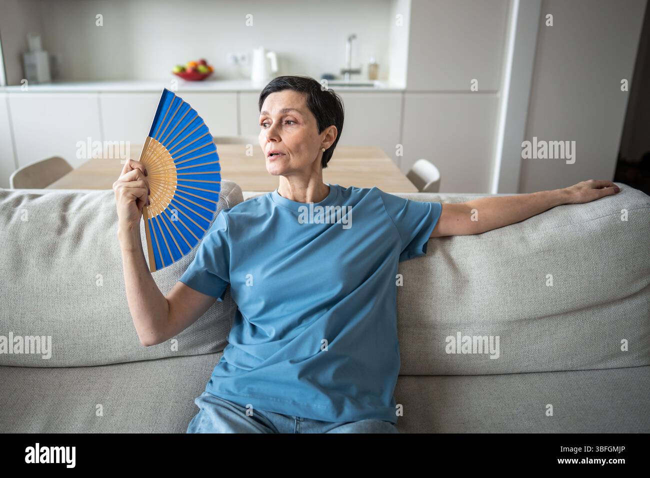 Exhausted mature woman fanning herself at home. Unbearable heat, elderly suffering from stuffy Stock Photo