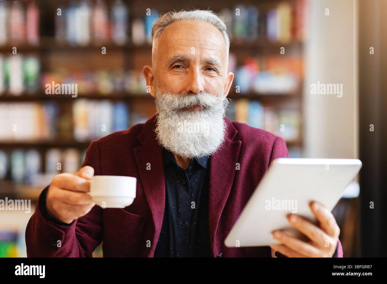 Wealthy senior businessman drinking coffee and using digital tablet Stock Photo