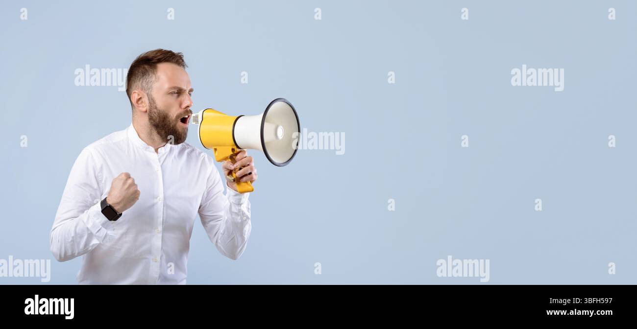 Agitated young man screaming into megaphone on grey studio background Stock Photo