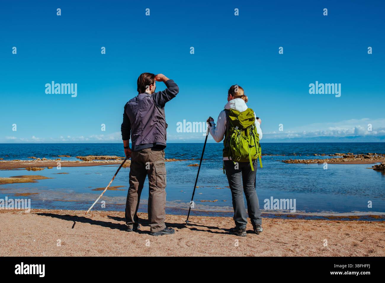 Man and woman tourists standing on lake shore and looking into the distance Stock Photo