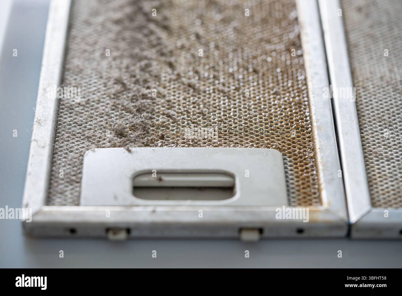 Greasy metallic exhaust filter needing deep cleaning. Placed on countertop for hygiene improvement Stock Photo